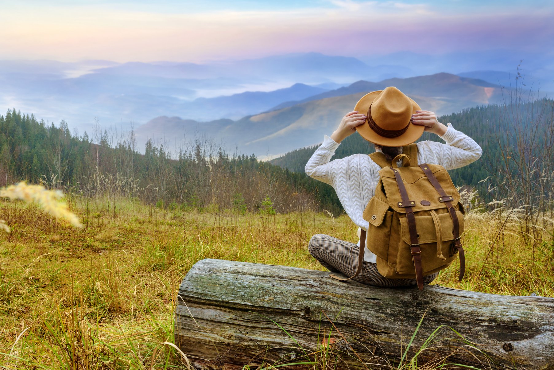 Woman traveler with backpack enjoying sunset on peak of mountain.